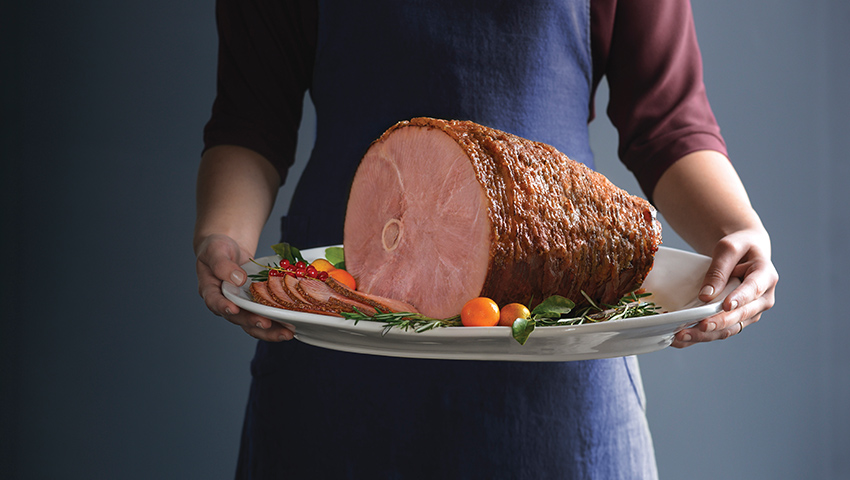 Sliced HoneyBaked Ham on plate held by home-cook.