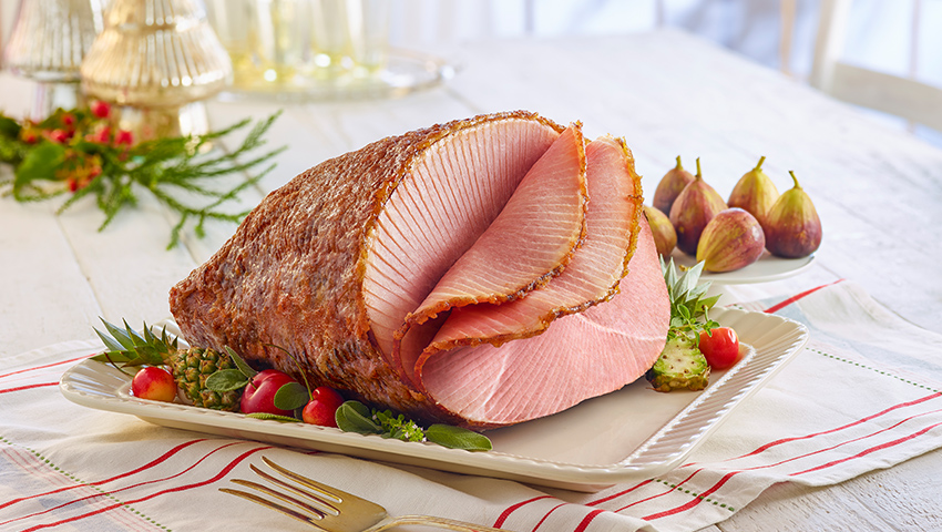 Sliced HoneyBaked Ham dressed on table on holiday spread.