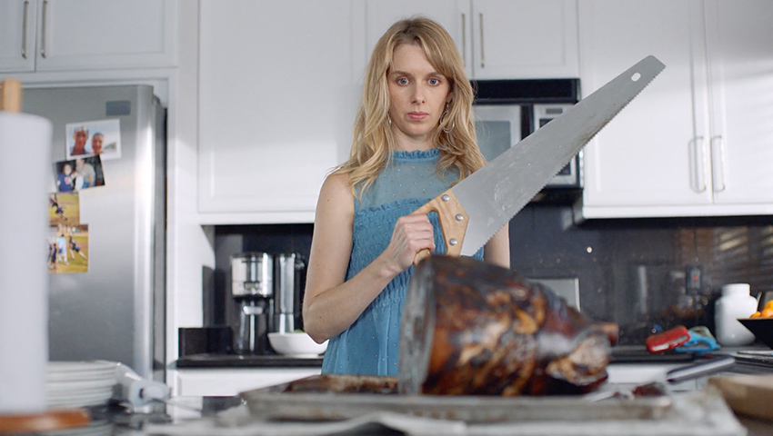KellyBaked Ham ad video screenshot: female burnt ham with saw in her kitchen.