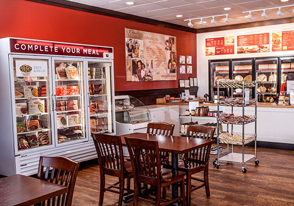 Interior photo of franchised Dawsonville, GA Honey Baked Ham store with fridges with products, tables, registers and the menu on the back wall.