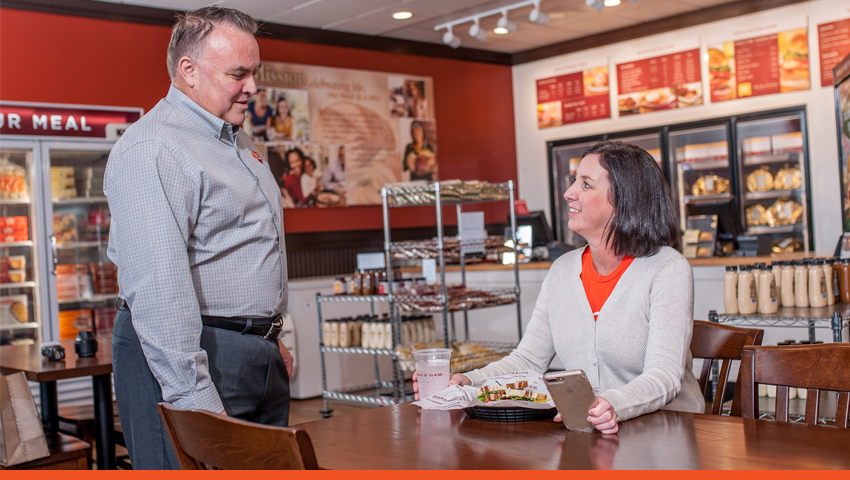 Standing man smiling at seated woman with food.