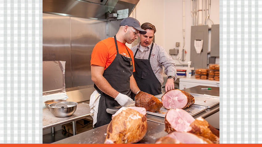 Image of two HoneyBaked employees in the kitchen preparing to cut ham